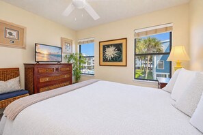 Habitación de hotel con una cama grande, televisión, cómoda y ventana con vistas a edificios y palmeras.