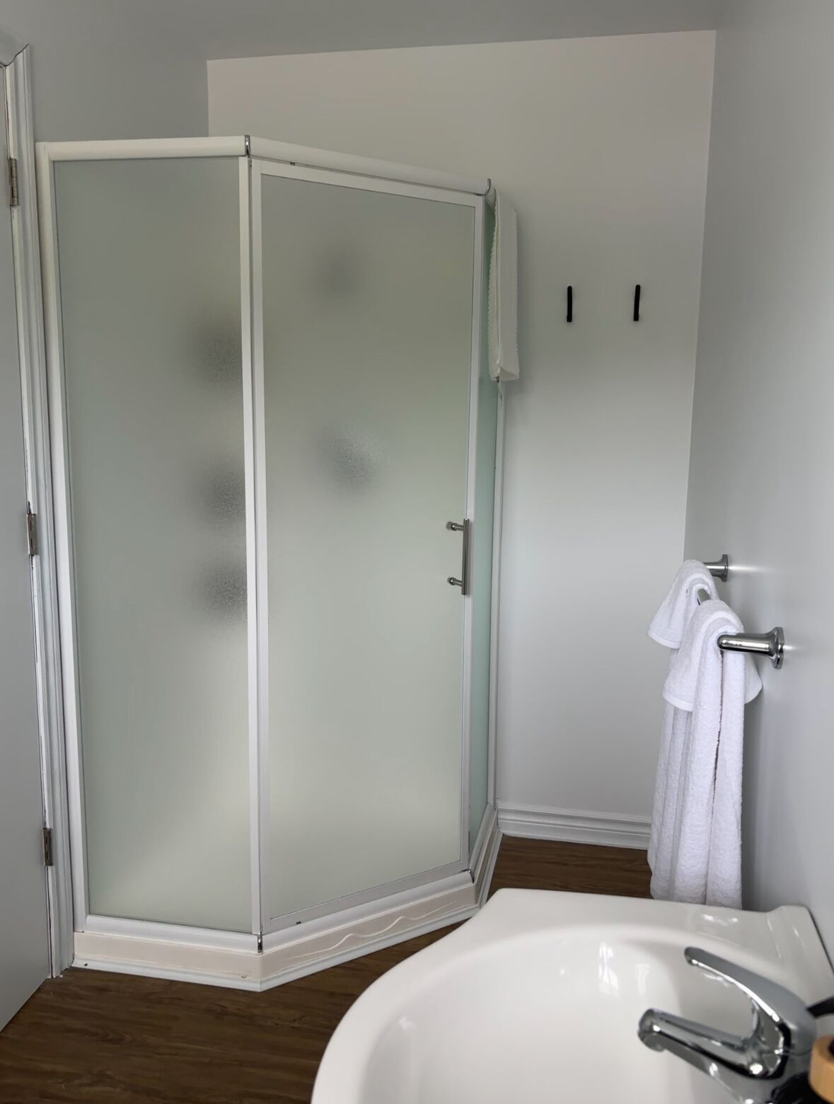 A modern bathroom with a glass-enclosed shower, a white sink, and a towel rack.