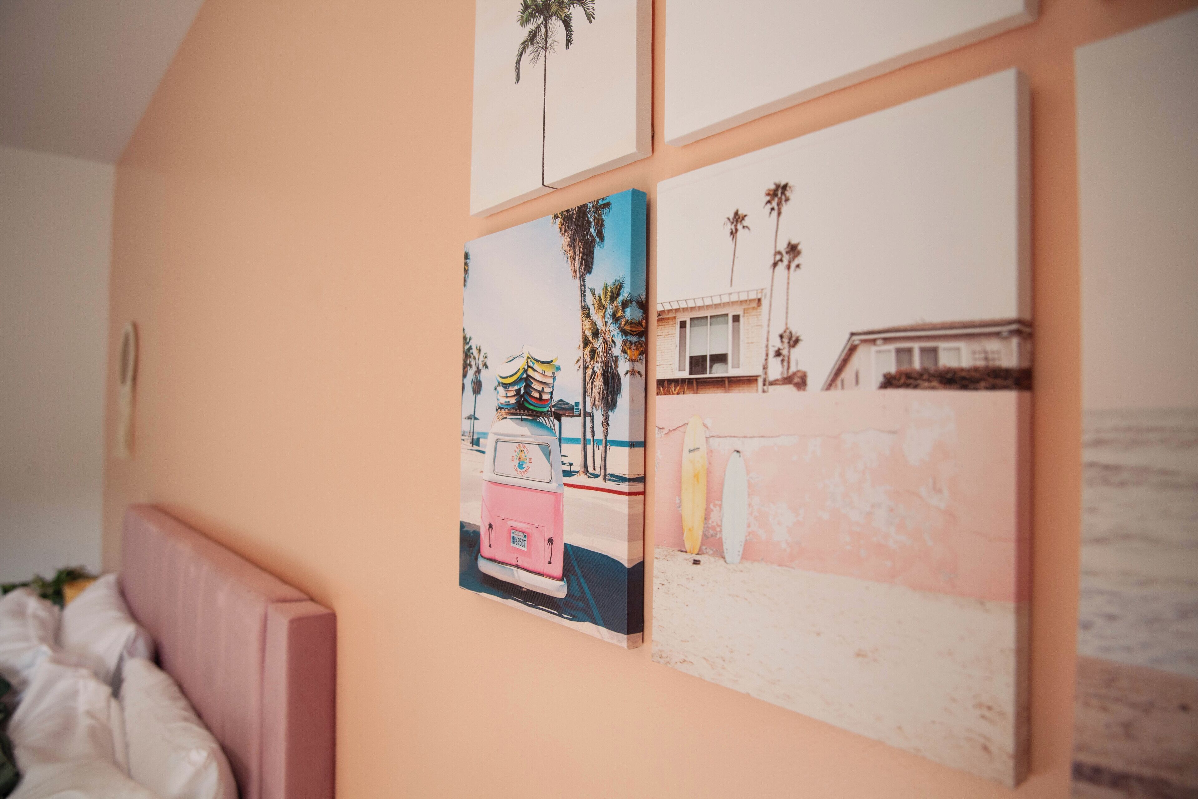 Un mur orné de quatre tableaux encadrés représentant des scènes de plage, dont un van rose et des planches de surf.