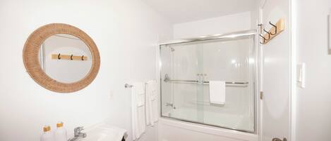 Un baño moderno con espejo redondo, lavamanos blanco y cabina de ducha de vidrio.