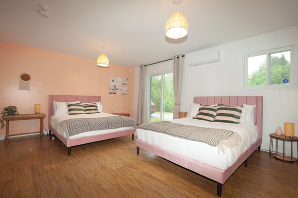Un dormitorio con dos camas, suelo de madera, una ventana con cortinas y una mesita de noche con lámpara.