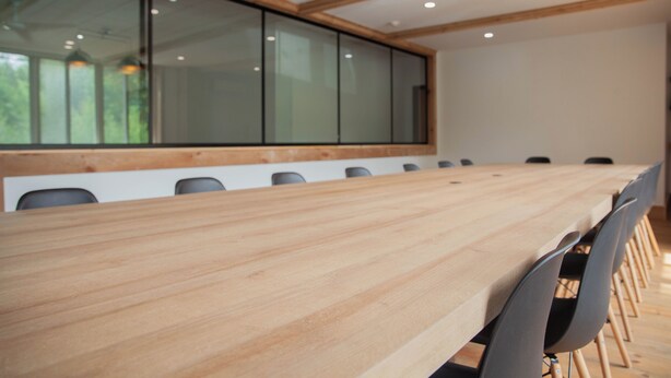 A conference room with a long wooden table, black chairs, and a large window with glass panels. - Hotel Le Riviera (Rawdon)
