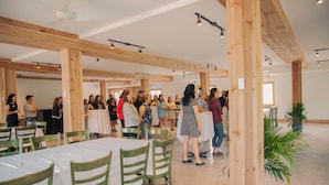 A spacious indoor venue with high wooden beams, green chairs, and tables arranged for a gathering. - Hotel Le Riviera (Rawdon)
