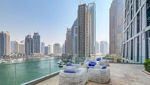 A rooftop terrace with wicker furniture and a view of a city skyline and marina. - Iconic Marina Stay Cayan Tower 2BR (Dubai)
