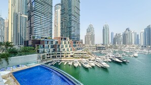 A marina with numerous boats docked, surrounded by high-rise buildings and a swimming pool area with lounge chairs. - Iconic Marina Stay Cayan Tower 2BR (Dubai)