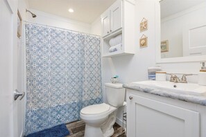 Een badkamer met een douchegordijn met patroon, een toilet, een wastafel met een marmeren blad en een spiegel boven de wastafel.