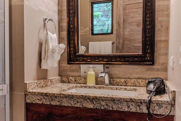 A bathroom with a granite countertop, a sink, a mirror, and a hairdryer.
