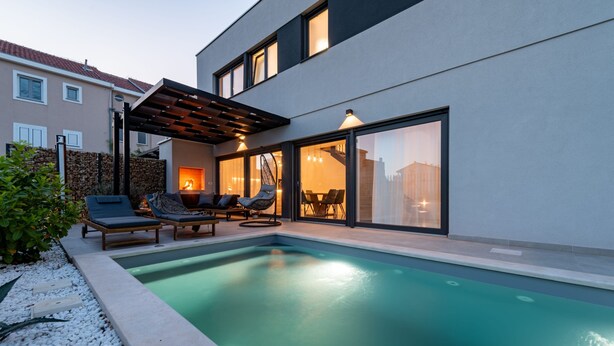 Un área de piscina moderna al aire libre con sillones de descanso, una pérgola y un comedor con vistas a la ciudad.