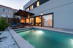 A modern outdoor pool area with lounge chairs, a pergola, and a dining area with a view of the cityscape. - Villa Cvita Zadarvillas (Privlaka)