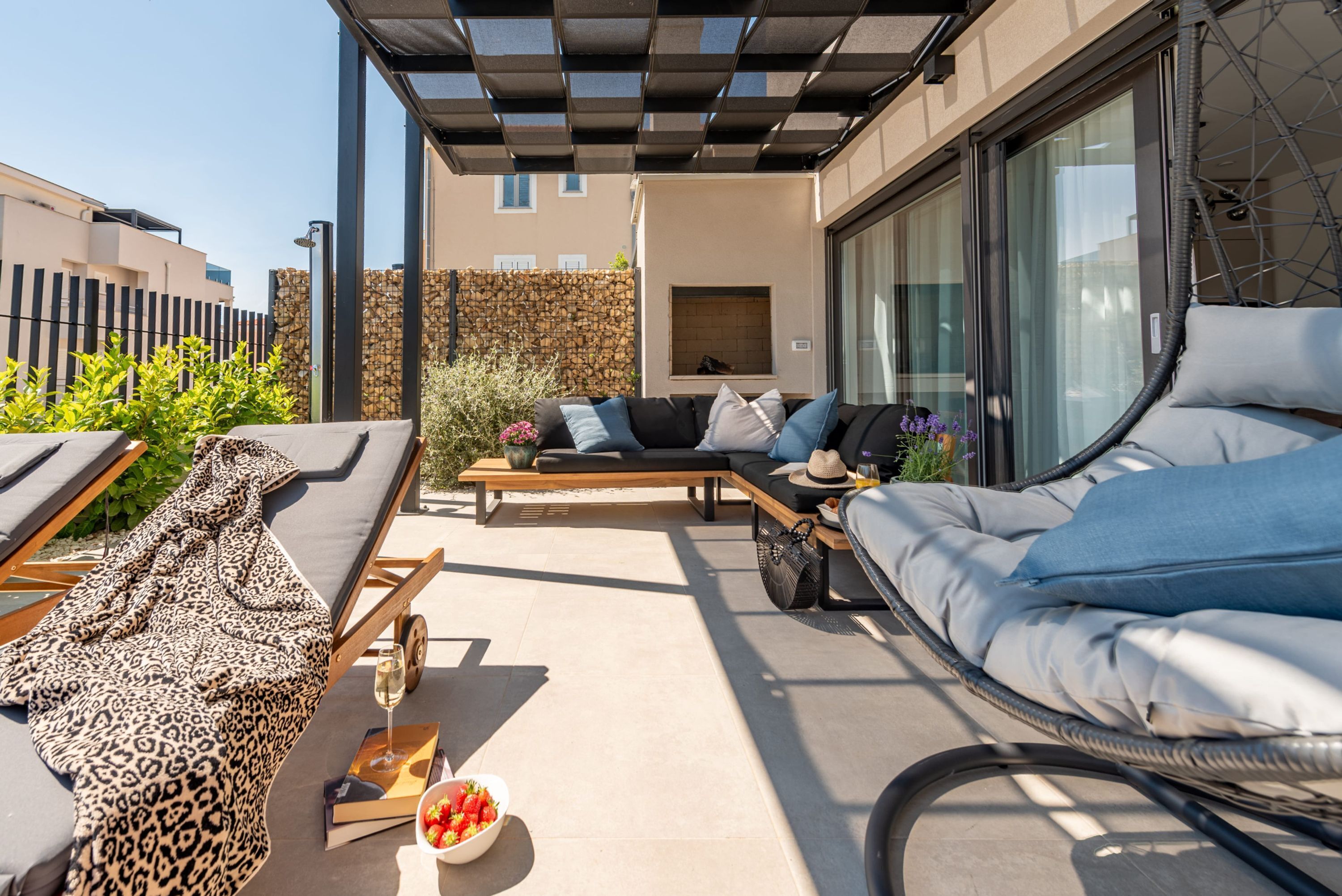 A modern outdoor lounge area with a sofa, a dining table, and a covered seating area.