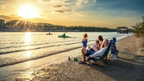 A beach scene with a sunset, a couple and a child in a beach chair, and a green boat in the water.