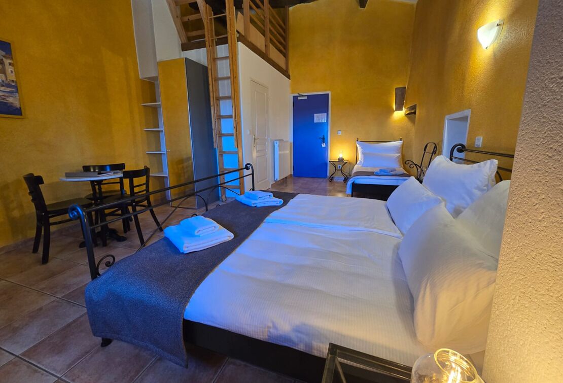 Ein Schlafzimmer mit Bett, Schreibtisch, Stuhl, einer Leiter und einer Tür.