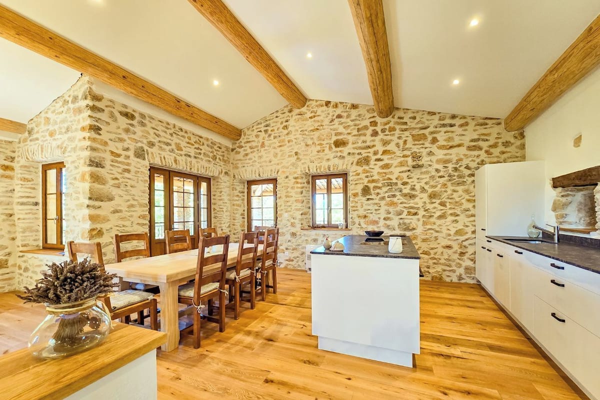 A rustic kitchen with stone walls, wooden beams, and a central island.