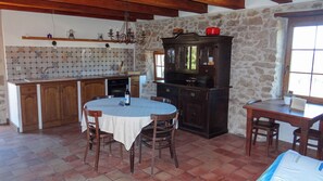 A kitchen with a dining table, chairs, a chandelier, and a stone wall. - Domaine du Frigoulet (Vagnas)