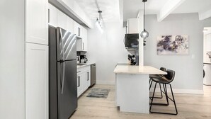 A modern kitchen with white cabinets, a stainless steel refrigerator, a microwave, and a coffee maker. There is a bar area with a stool and a pendant light. - Beautiful remodeled 1-bedroom condo in Littleton/ Englewood with Pool (Englewood)