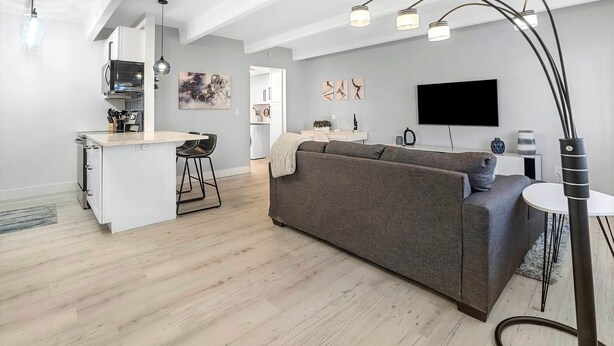 A modern living space with a kitchen, dining area, and seating area. It includes a sofa, a dining table, and a TV mounted on the wall. - Beautiful remodeled 1-bedroom condo in Littleton/ Englewood with Pool (Englewood)