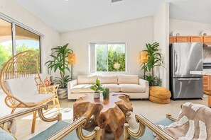 A modern living room with a sofa, a wooden coffee table, and a wicker chair. There is a kitchen area with a refrigerator and cabinets. - Tulum Vibes in Desert Boho • Hideout • Pool • Spa (Desert Hot Springs)