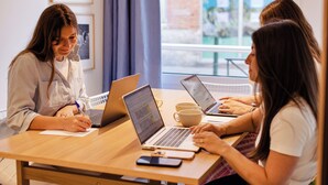 Three individuals seated at a table with laptops, a smartphone, and a cup, in a room with framed pictures on the wall. - Alfred Hotels Toulouse Centre Wilson - Hôtel Rénové  (Toulouse)