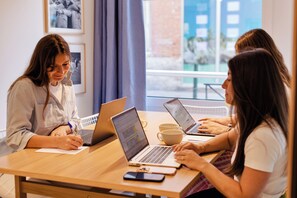 Three individuals seated at a table with laptops, a smartphone, and a cup, in a room with framed pictures on the wall. - Alfred Hotels Toulouse Centre Wilson - Hôtel Rénové  (Toulouse)