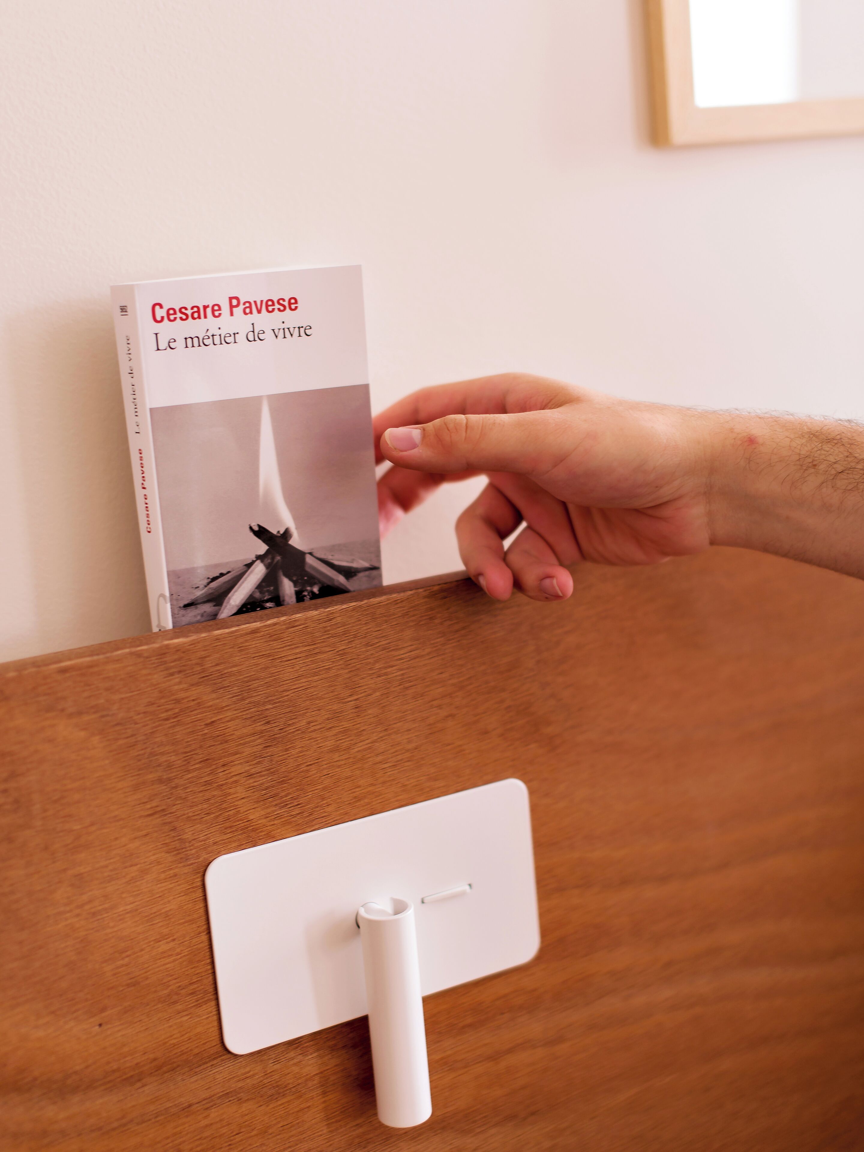 A hand holding a book titled "Le métier de vivre" by Cesare Pavese.