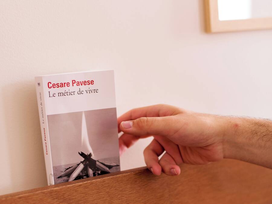 A hand holding a book titled "Le métier de vivre" by Cesare Pavese.