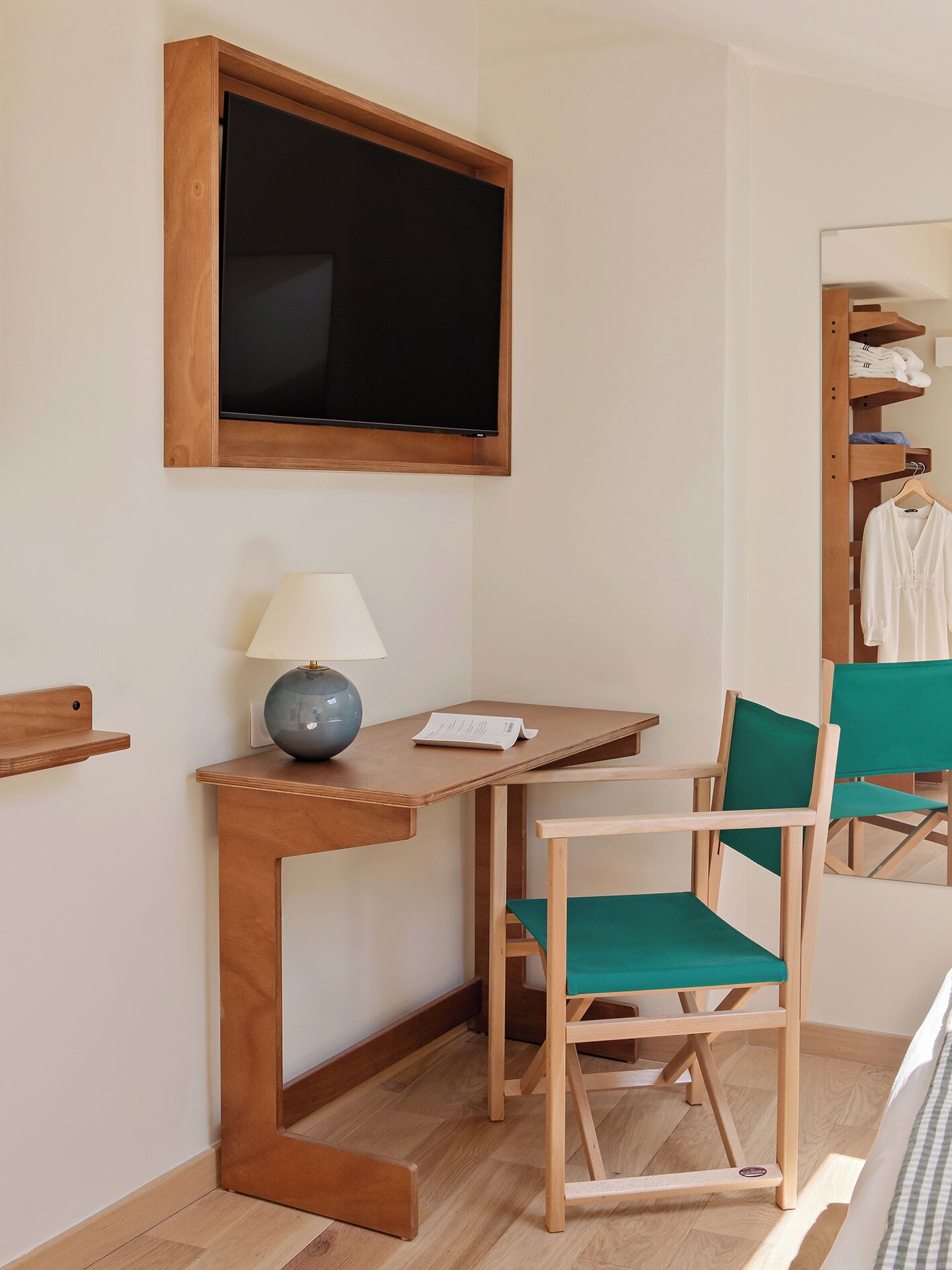 A room with a wooden desk, a chair, a lamp, a television, and a clothing rack.