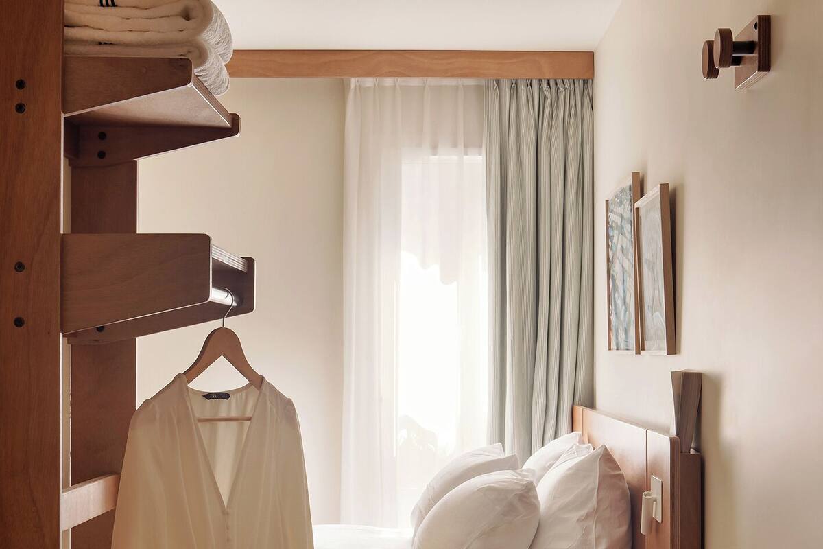 Ein Schlafzimmer mit Bett, einer Kleiderstange, einem Nachttisch aus Holz und einem Fenster mit Vorhängen.
