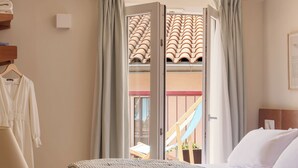Una habitación de hotel con cama, escritorio, silla, ventana con cortinas y vista a un edificio con tejado de tejas.