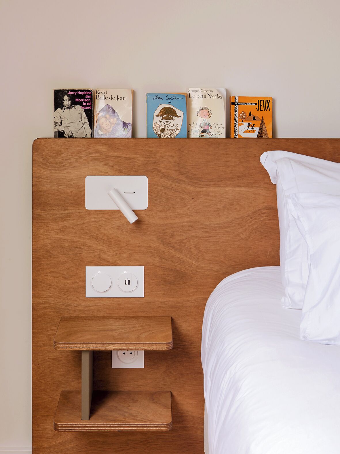 Una cama bien hecha con sábanas blancas y un cabecero con estante que exhibe libros.