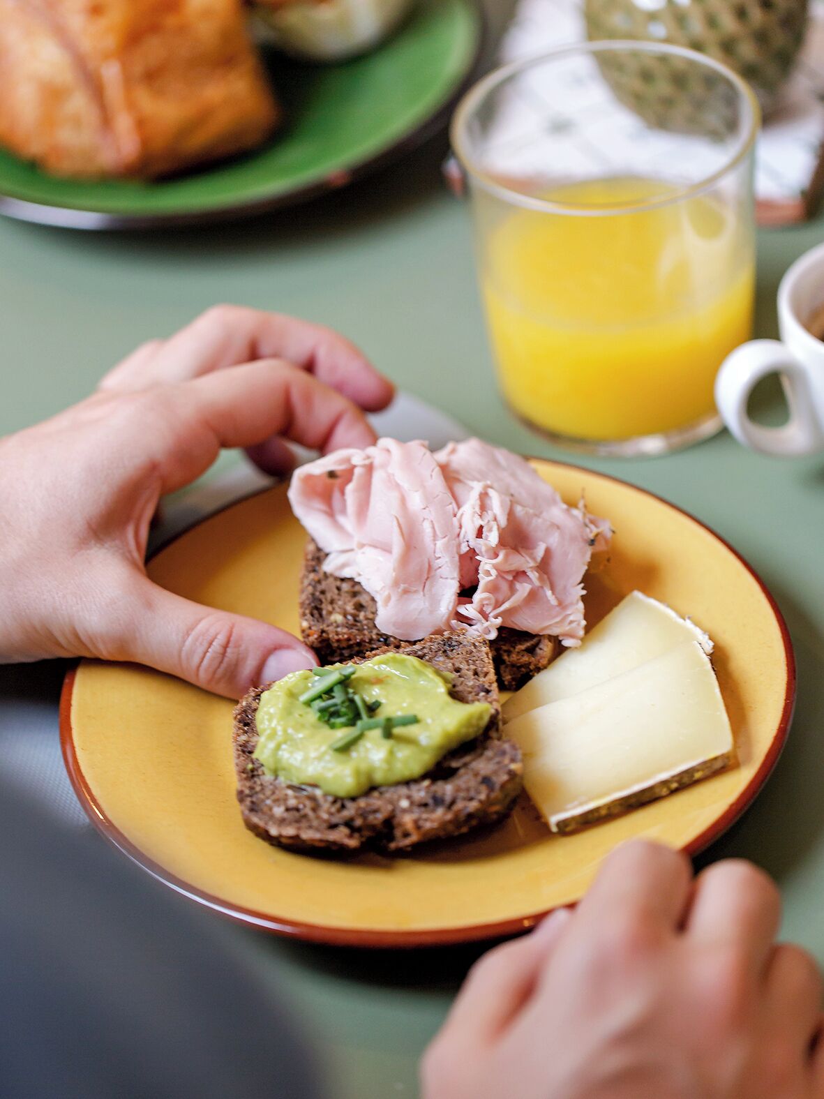 A plate with a slice of bread topped with avocado, cheese, and meat.