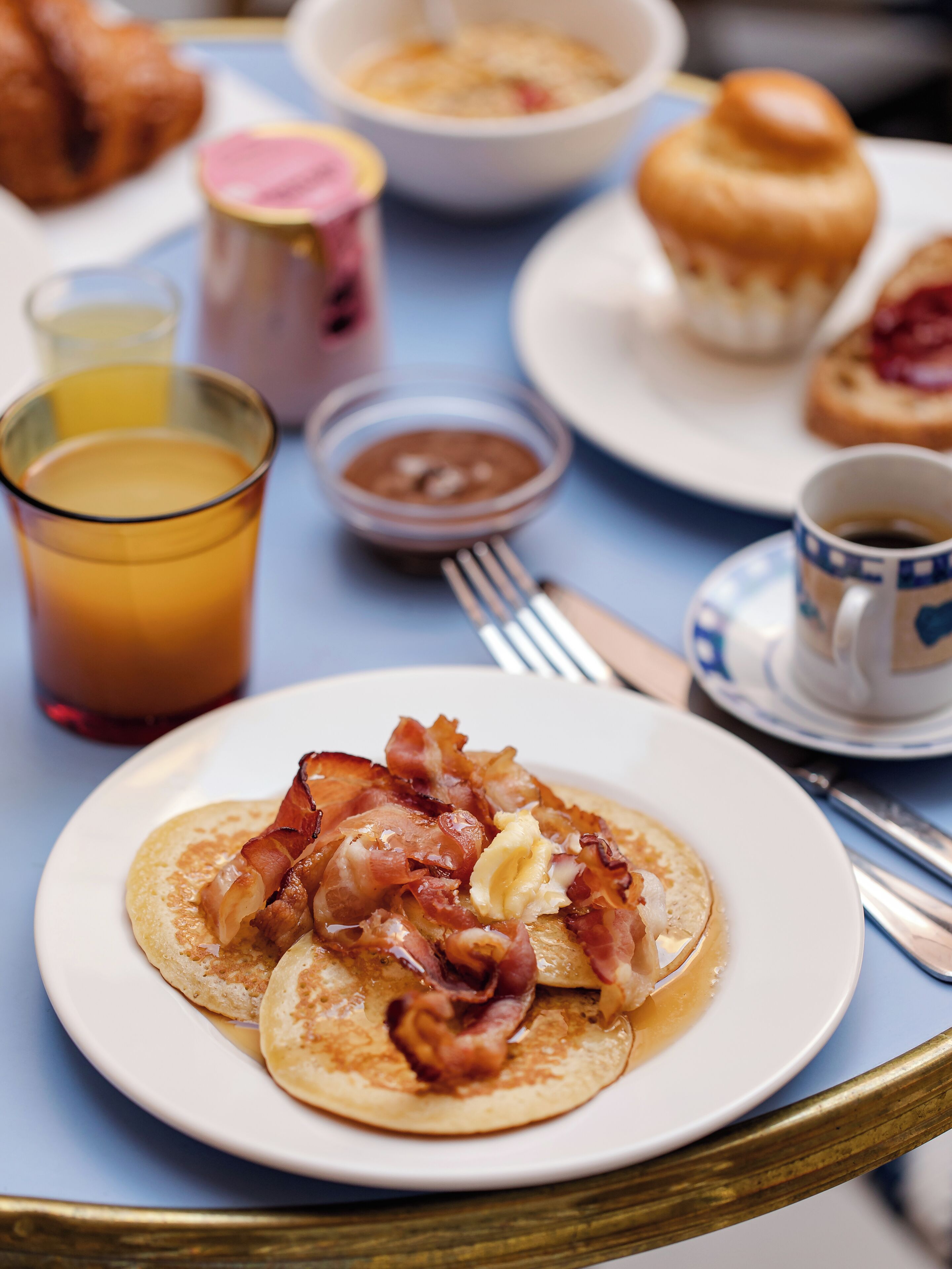 A breakfast table with pancakes, bacon, a cup of coffee, and a glass of orange juice.