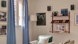 A living room with wicker furniture, a floor lamp, and a bookshelf with books and decorative items. - Alfred Hotels Toulouse Centre Wilson - Hôtel Rénové  (Toulouse)