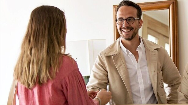 A man and a woman shaking hands in a hotel lobby with a wooden reception desk and a large mirror. - Alfred Hotels Toulouse Centre Wilson - Hôtel Rénové  (Toulouse)