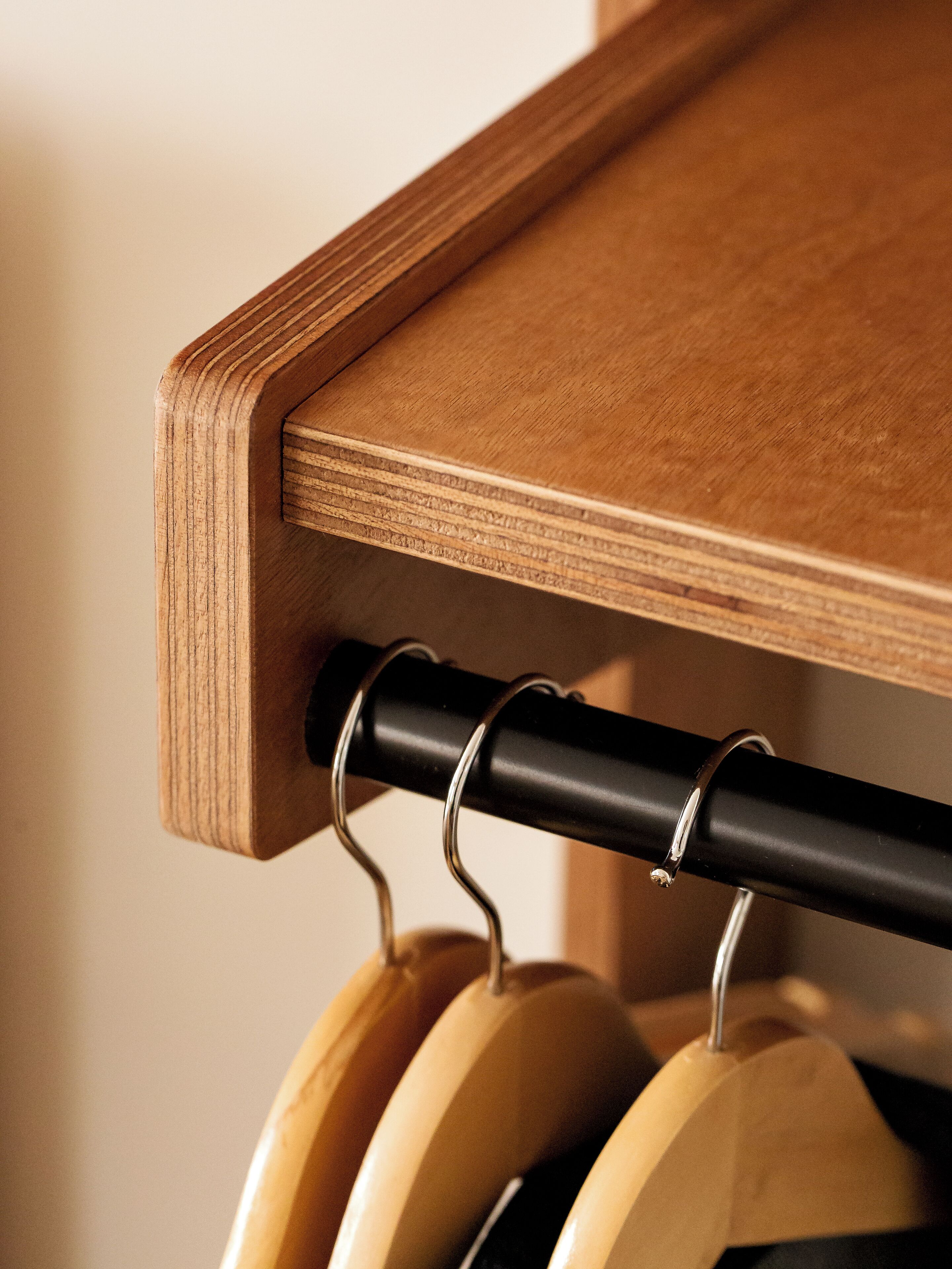 A wooden shelf with a black metal rod and wooden hangers.