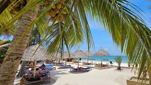 A beach with thatched umbrellas, lounge chairs, and palm trees. - Kae Beach Resort (Michamvi)