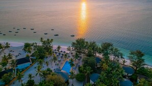 An aerial view of a beach resort with a swimming pool, palm trees, and boats on the water. - Kae Beach Resort (Michamvi)