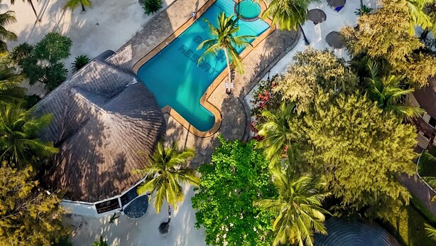 An aerial view of a beach resort with a swimming pool, palm trees, and boats on the water. - Kae Beach Resort (Michamvi)
