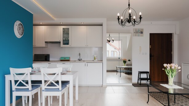 Una cucina moderna con mobili bianchi, un'area pranzo con sedie bianche, un lampadario nero e un orologio appeso al muro.