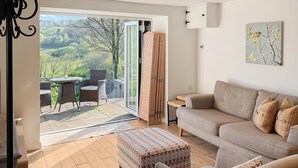 En stue med sofa, skammel og udsigt til en have gennem en skydedør.