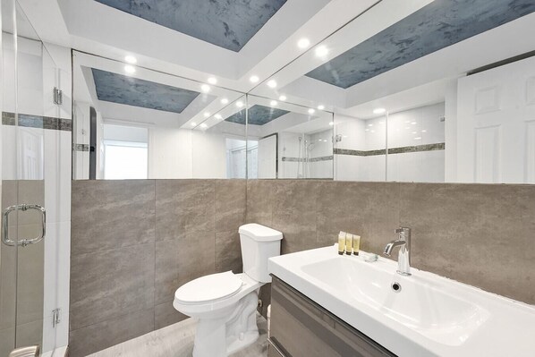 A modern bathroom with a large mirror, a bathtub, and a toilet.