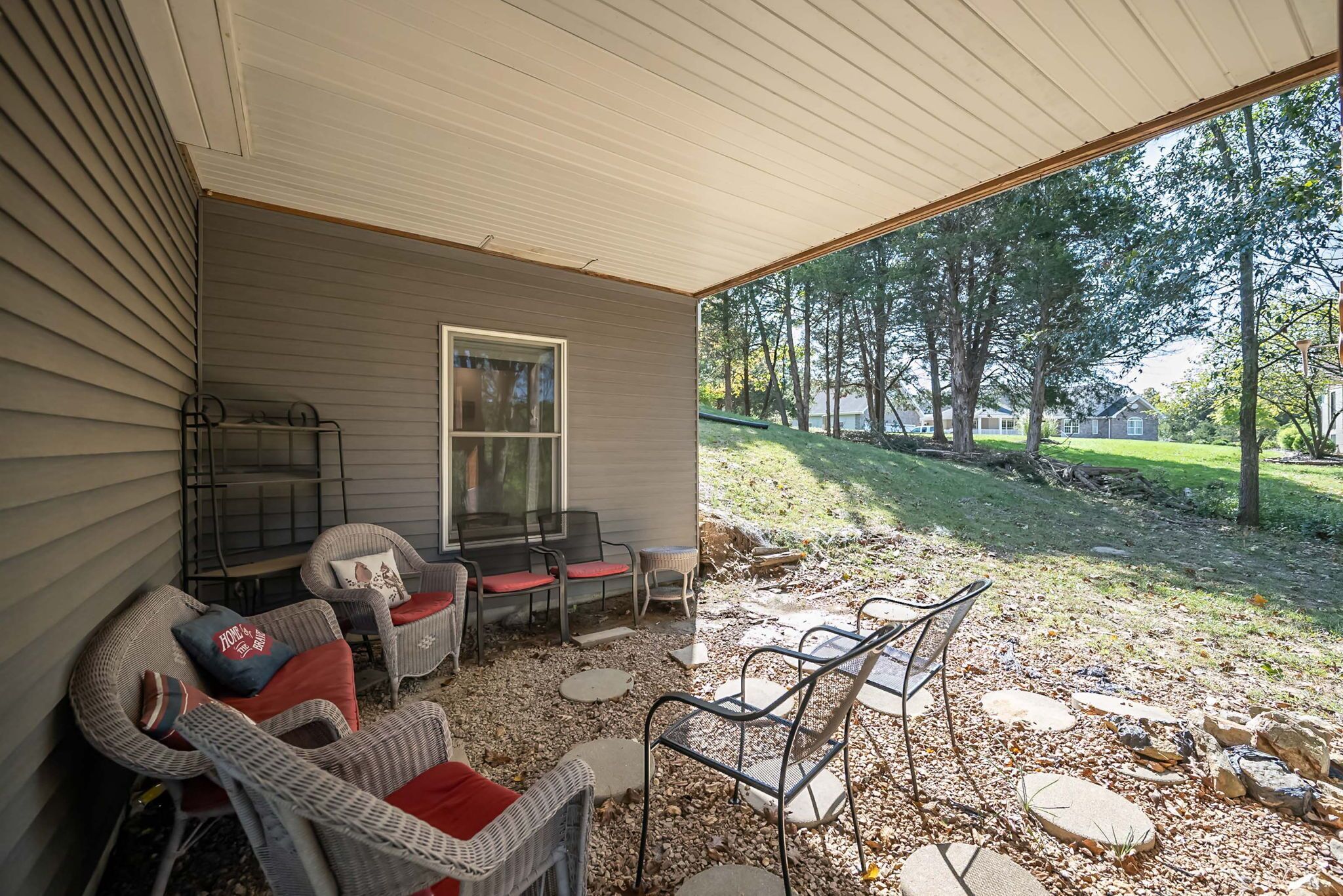 A covered patio area with wicker furniture and a view of a grassy yard.