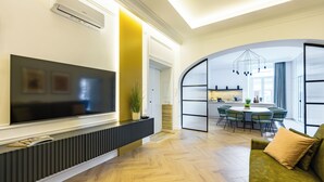A modern living room with a flat-screen TV, a sofa, and a dining area with a table and chairs.