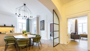 A modern kitchen with a wooden countertop, a dining area with a round table and green chairs, and a large window with curtains.