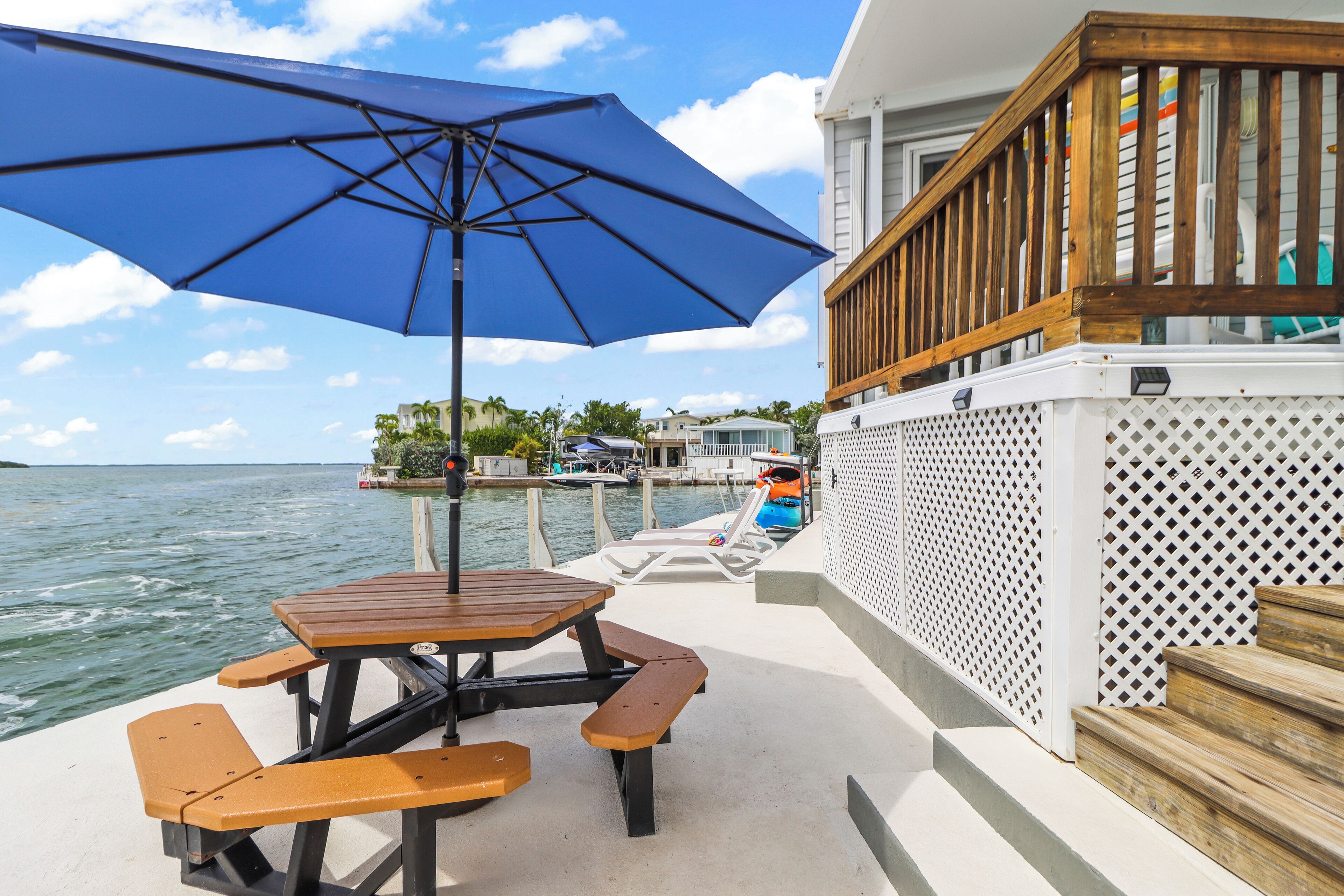 Um terraço com mesa para piquenique e bancos, com vista para um corpo d'água com barcos e casas ao fundo.