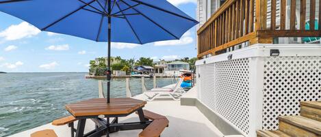 Um terraço com mesa para piquenique e bancos, com vista para um corpo d'água com barcos e casas ao fundo.
