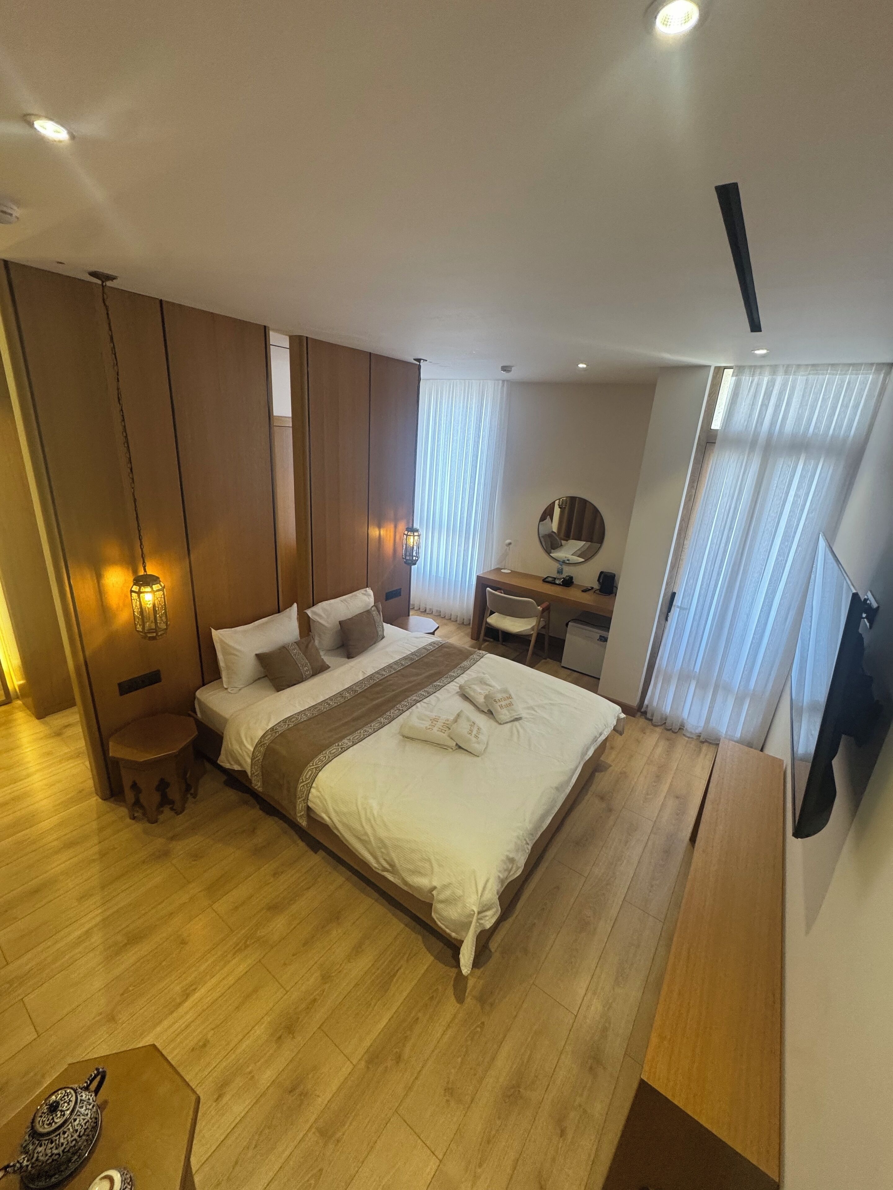 Une chambre d’hôtel moderne dotée d’un grand lit, d’un plancher en bois, d’un bureau avec une chaise, d’un téléviseur fixé au mur et d’une petite table agrémentée d’un objet décoratif.