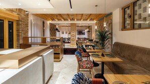 A modern dining area with wooden tables and chairs, a reception desk, and a seating area with a sofa. - Sarhad Hotel (Bukhara)