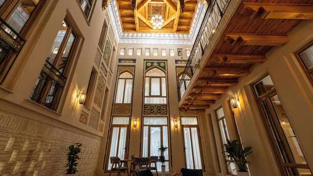 A spacious lobby with high ceilings, ornate wooden beams, and large windows with intricate designs. - Sarhad Hotel (Bukhara)