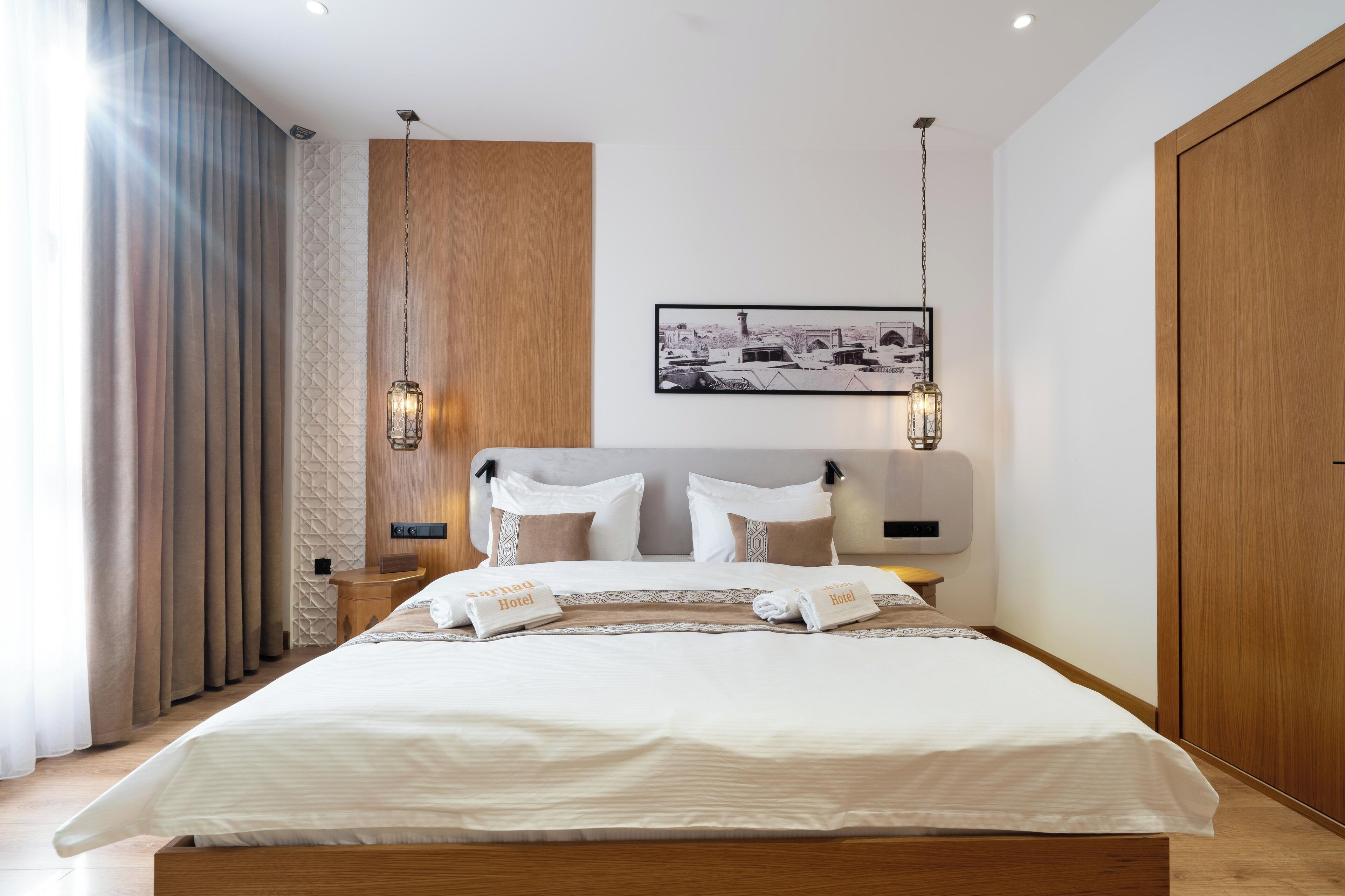 A modern hotel room with a large bed, wooden headboard, and a framed picture on the wall.