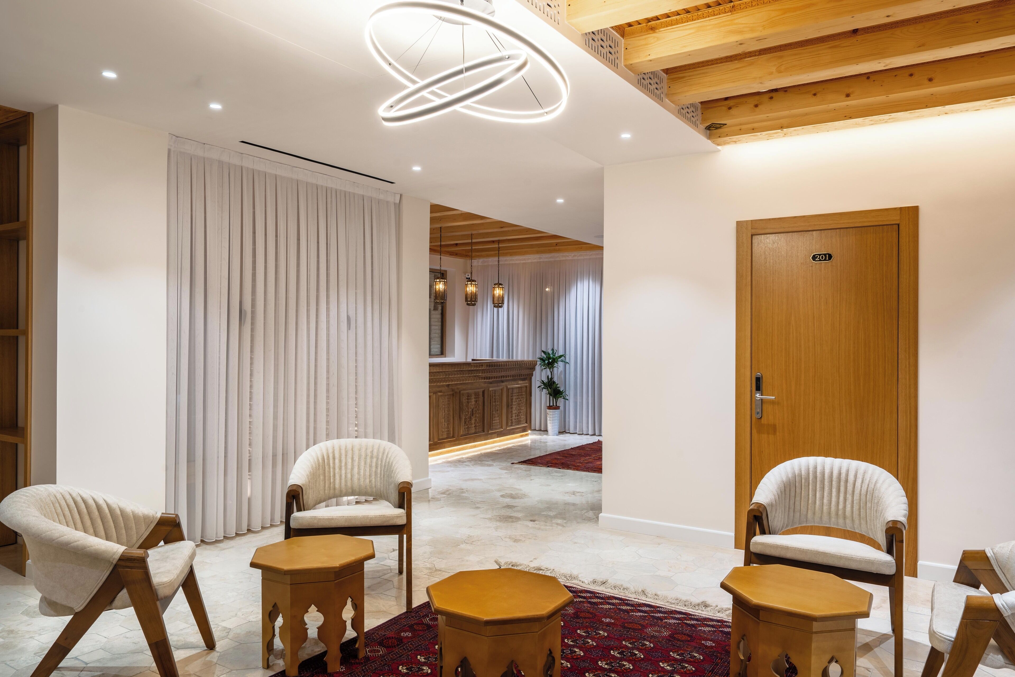 Eine Hotelhalle mit einem hölzernen Empfangsbereich, einer Holztür mit der Nummer 201 und drei Polsterstühlen mit kleinen Holztischen.